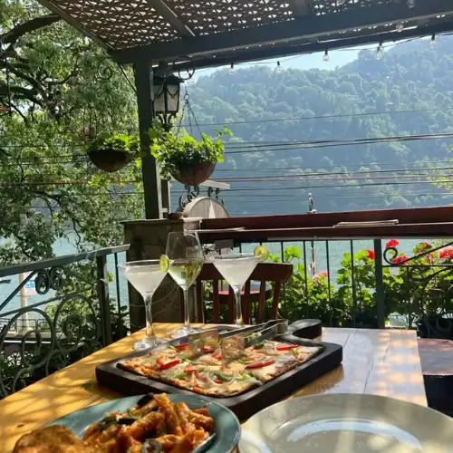 Outdoor cafe table with pizza, pasta, and drinks overlooking the scenic Naini Lake in Nainital.