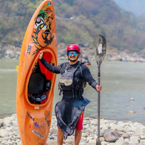 Kayaker standing by the Ganga River in Rishikesh holding a paddle and orange kayak