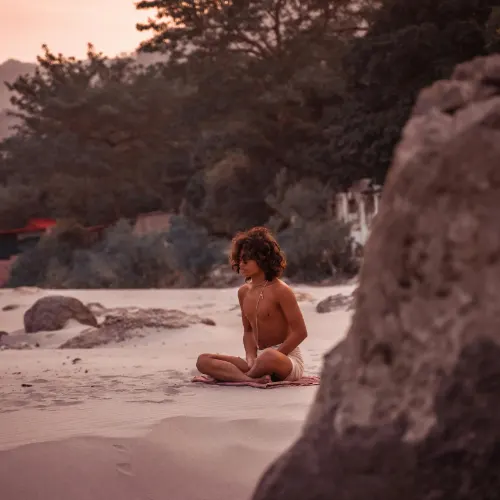 Man meditating on the sandy banks of the Ganga during a peaceful sunrise in Rishikesh, India.