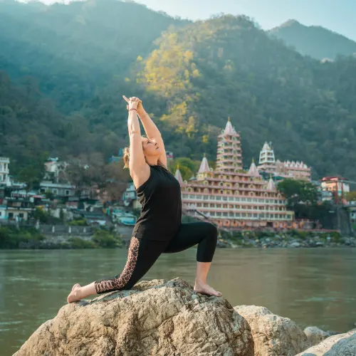 Woman practicing yoga by the Ganga River with iconic Rishikesh temples in the background – Yoga Capital of the World.