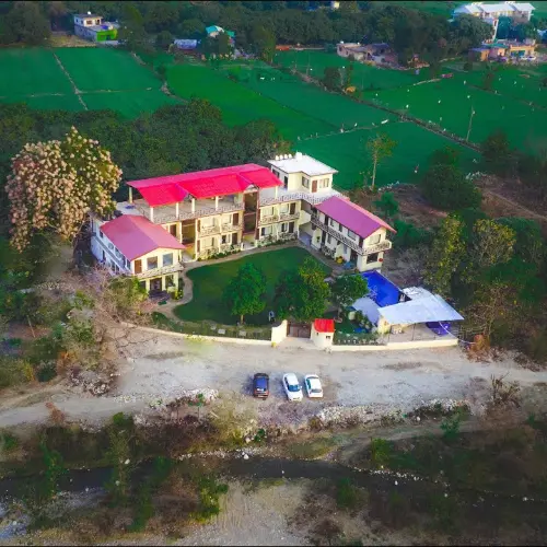 Aerial view of a countryside eco-resort surrounded by green fields and forest near Ramnagar.