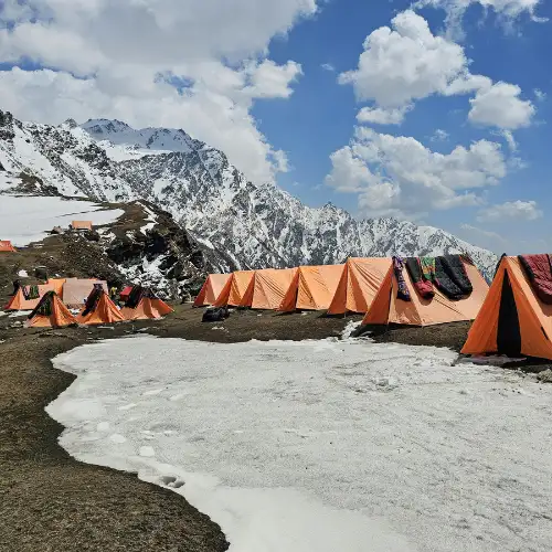 High-altitude campsite with orange trekking tents set up on a snowy mountain ridge during the Kyarkoti Trek in Uttarakhand.