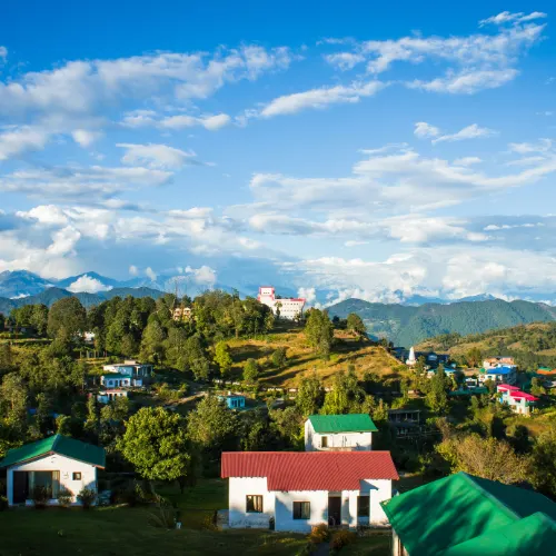 Scenic landscape view of Kausani with colourful houses, green hills, and distant mountains