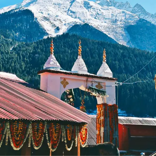 Himalayan temple decorated with flowers against a backdrop of snow-covered mountains near Harsil on the Kyarkoti Trek route.